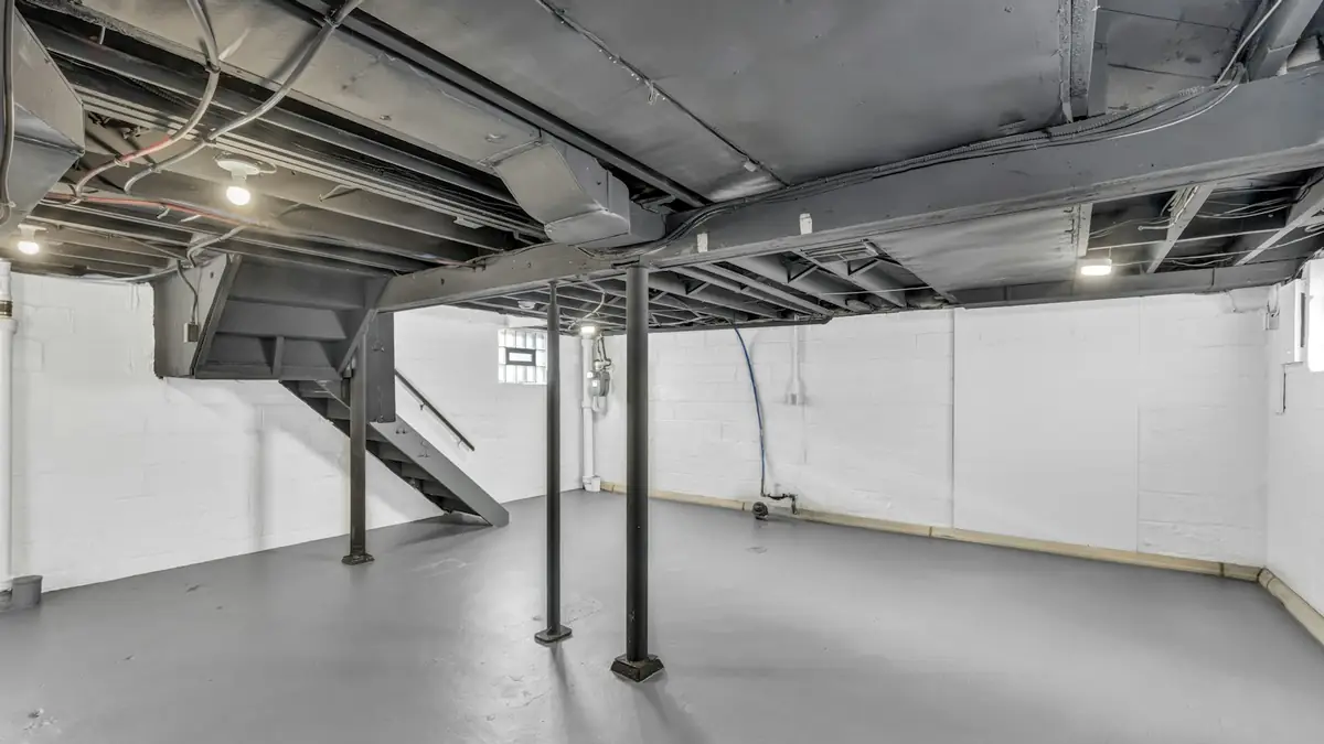 An empty unfinished basement with white walls, steel posts and exposed joists - Leak Detection in Derby