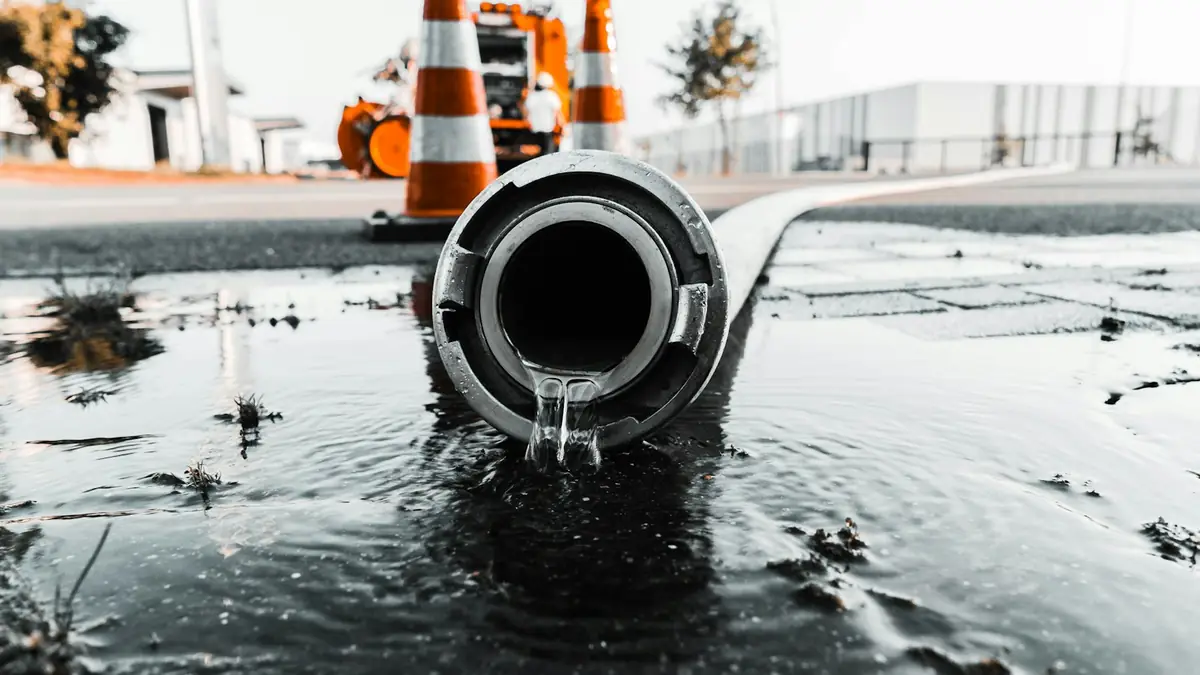 Water running from an open pipe end into a puddle, road cones behind - Leak Detection in Derby