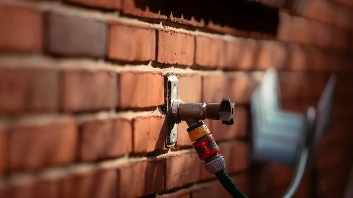 A garden hose connected to an outdoor tap on a red brick wall