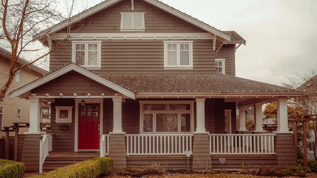 A two-story brown Craftsman house with a red door and white porch rail - Leak Detection in Commerce City